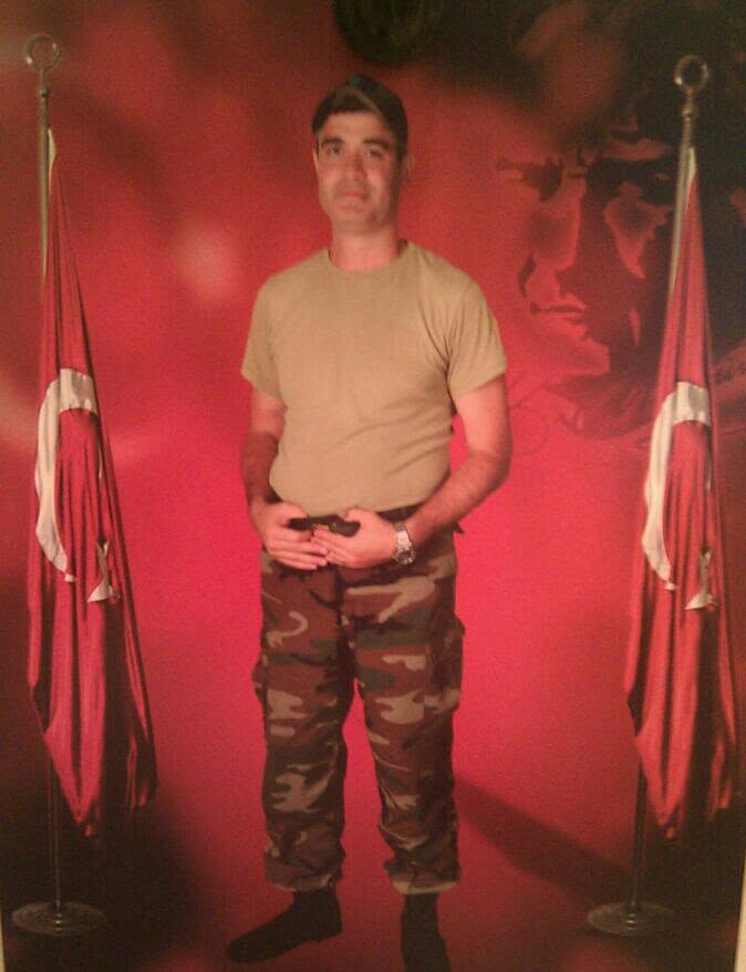Photograph of Fikri Ozcelik standing between two flags.