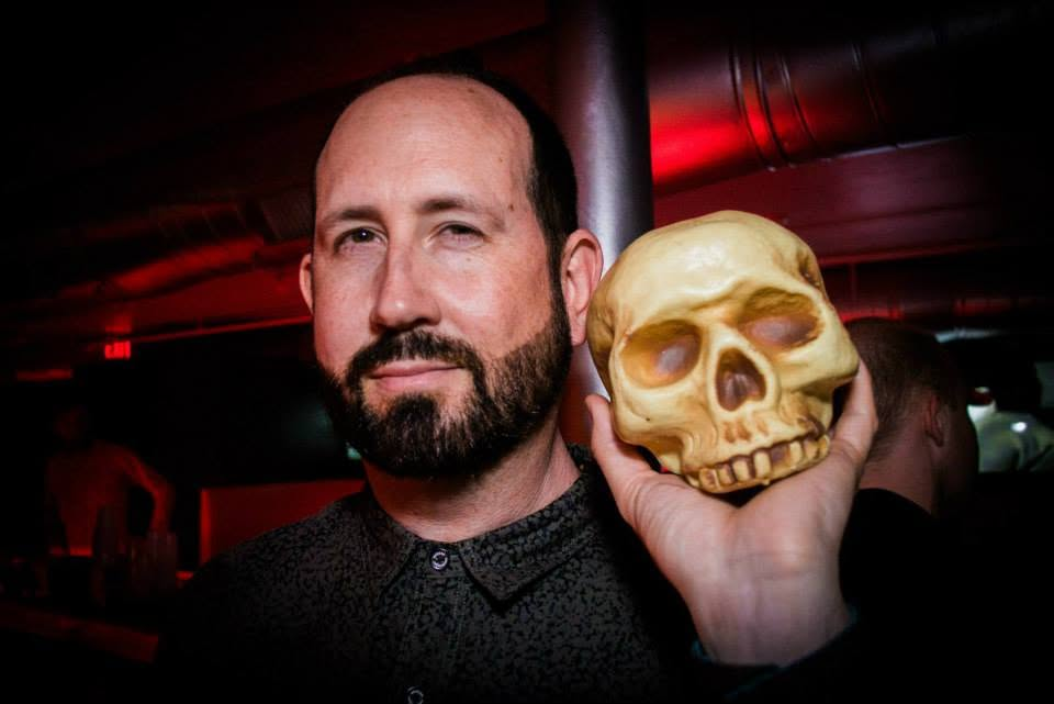 Portrait of DJ Damon Allen holding a skull prop at an indoor event.