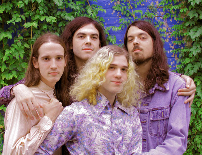 Group portrait of Featherface posed in front of green vines.