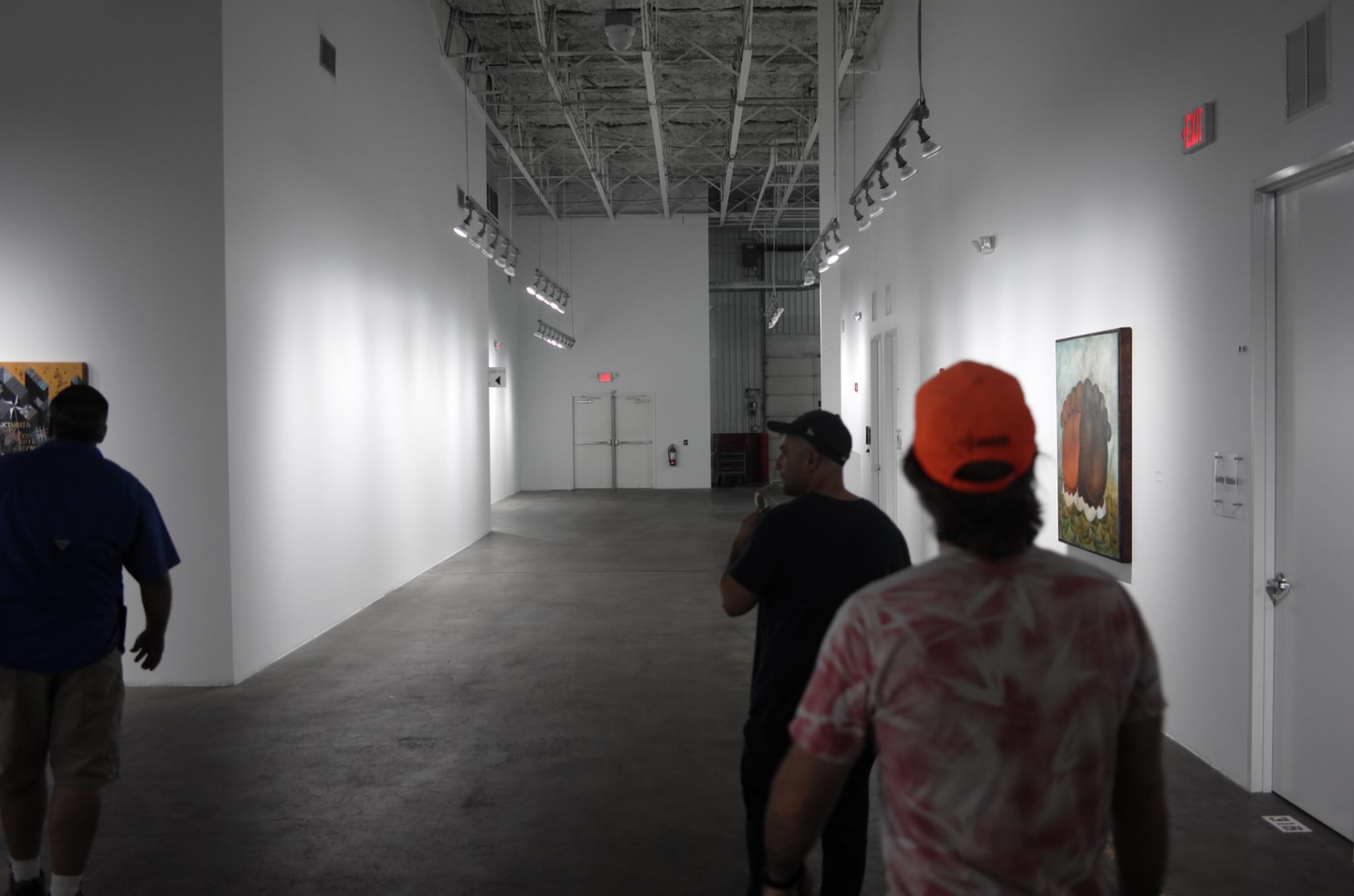 Three people walking a white-walled gallery corridor with hung paintings during the exploratory Day for Night 2015 site visit.