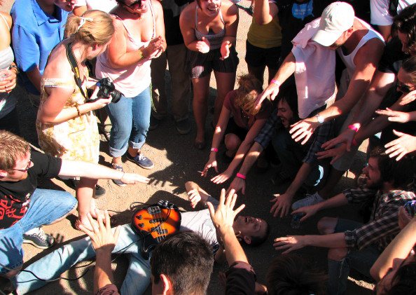 Crowd closing in around a guitarist performing on the ground at an outdoor Houston show