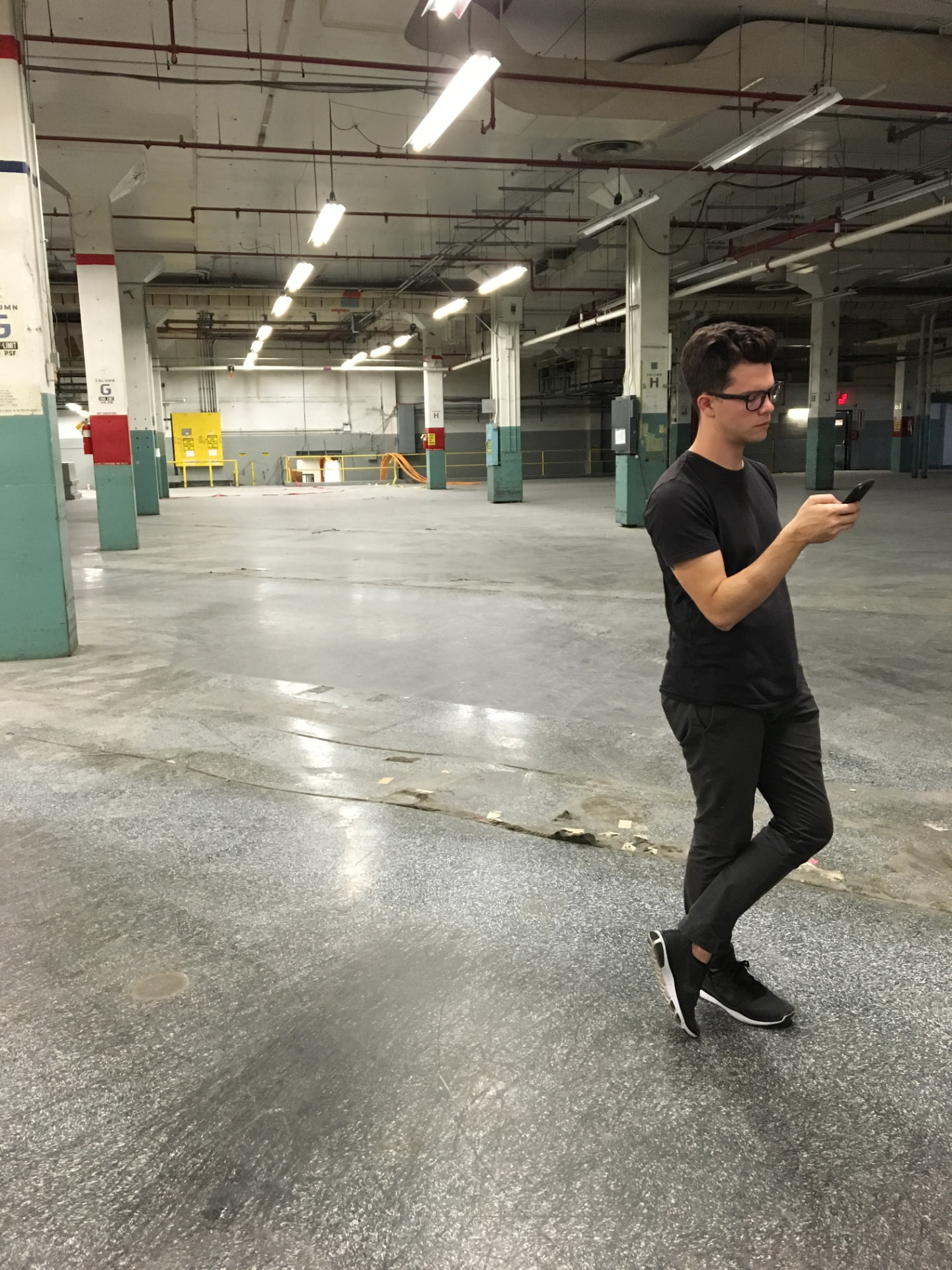 A person surveying the empty postal work floor, a phone in hand, with painted columns and rail lines visible across the ceiling.