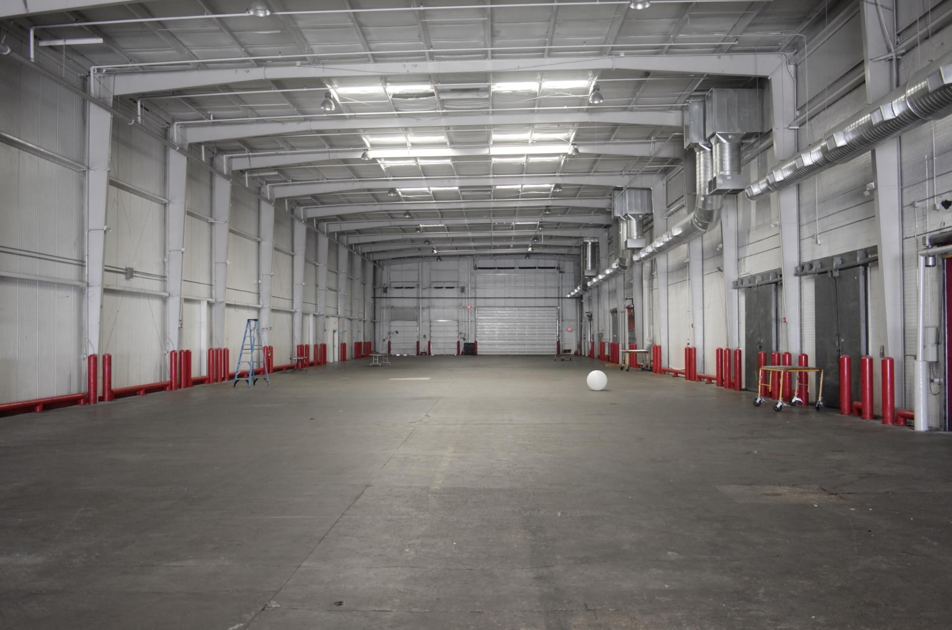 Empty lit warehouse hall lined with red bollards and loading doors during the exploratory Day for Night 2015 site visit.