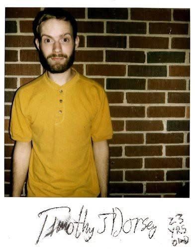 Signed Polaroid portrait of Timothy J. Dorsey in a yellow shirt against a brick wall.