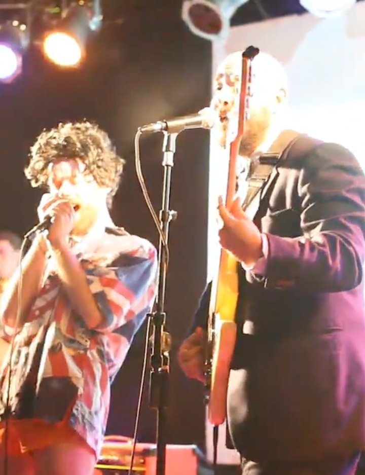 Delicious Milk performing live, harmonica and guitar at the microphone.
