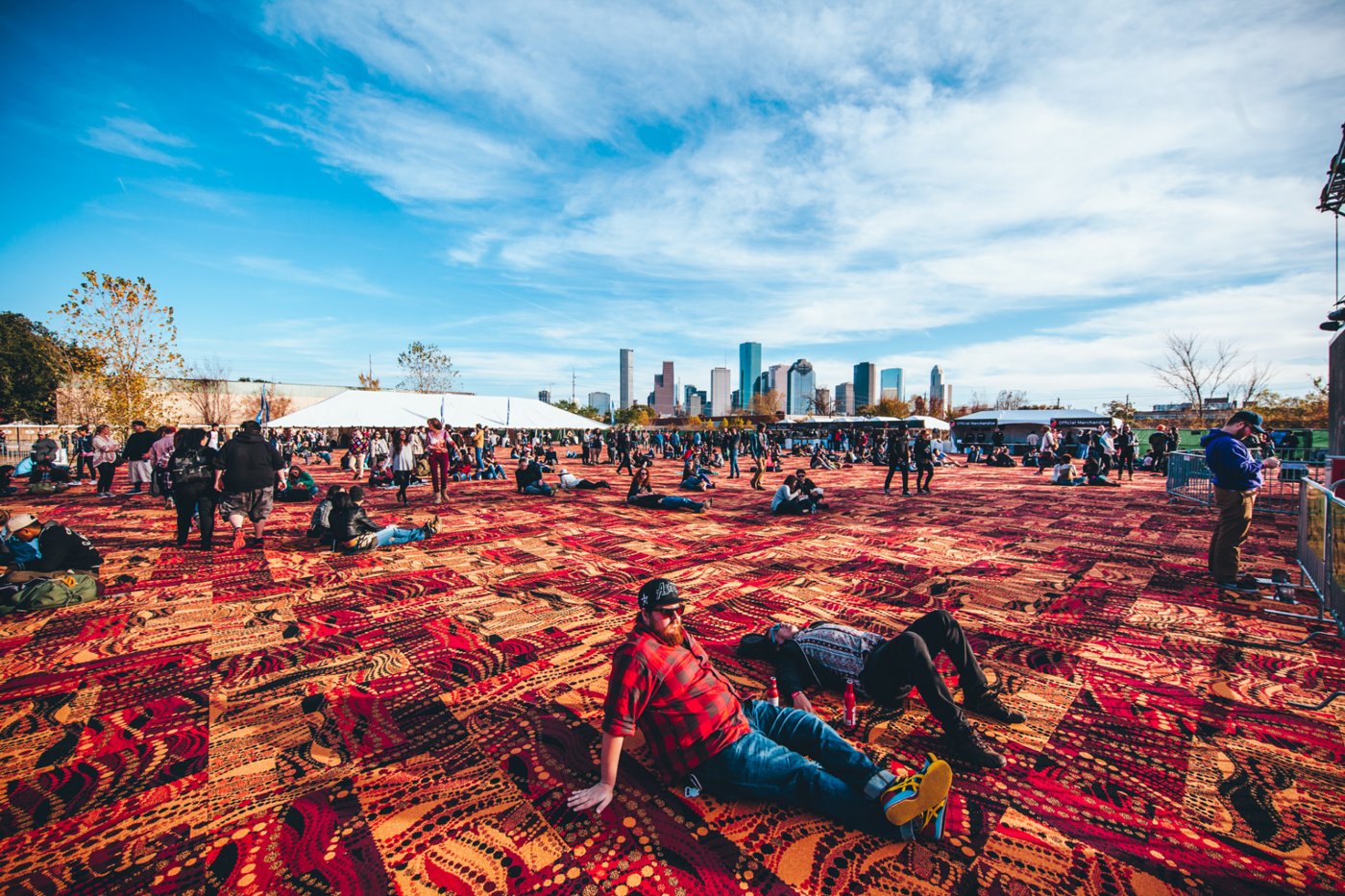 Festival grounds carpeted in red patterned rugs with the Houston skyline behind.